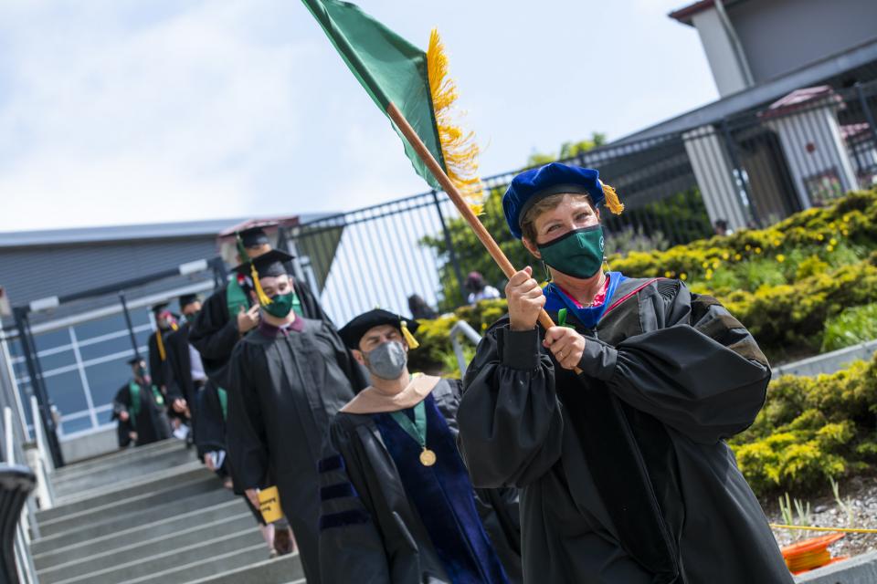 professor in graduation attire leading a group of students onto the field