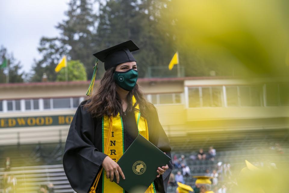 student walking in graduation robes holding diploma cover