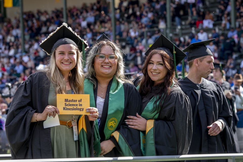 graduate students at commencement  holding a sign reading "Masters of Science Kinesiology"