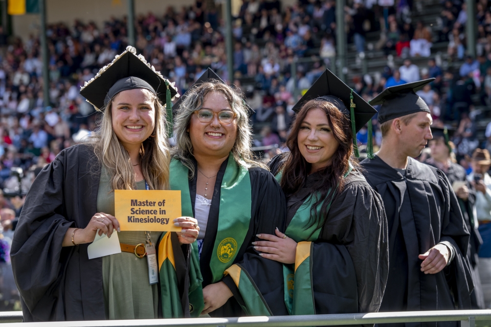 graduate students at commencement holding a sign reading "Masters of Science Kinesiology"