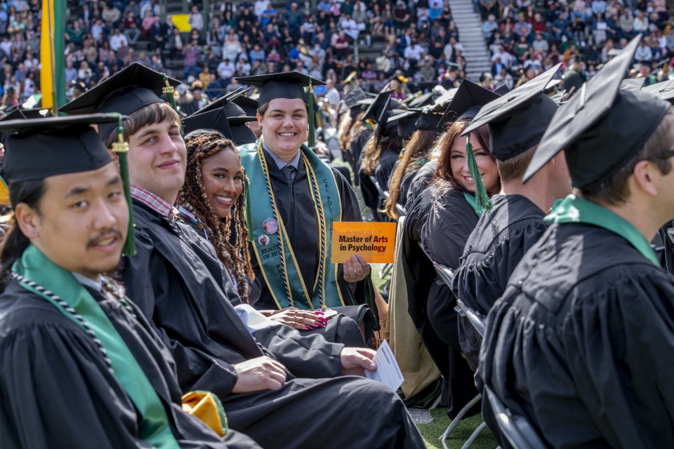 graduate students at commencement  holding a sign reading "Masters of Arts Psychology"