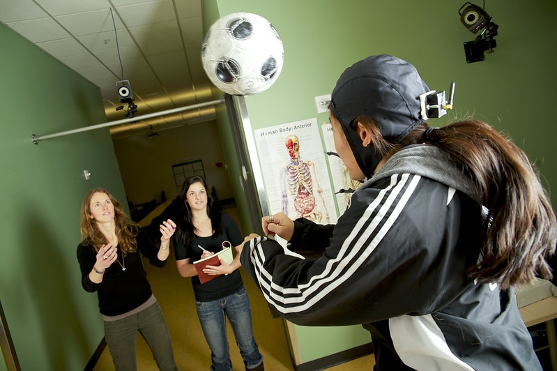 students in the kinesiology lab with one student wearing a cap to monitor the force of a soccer ball